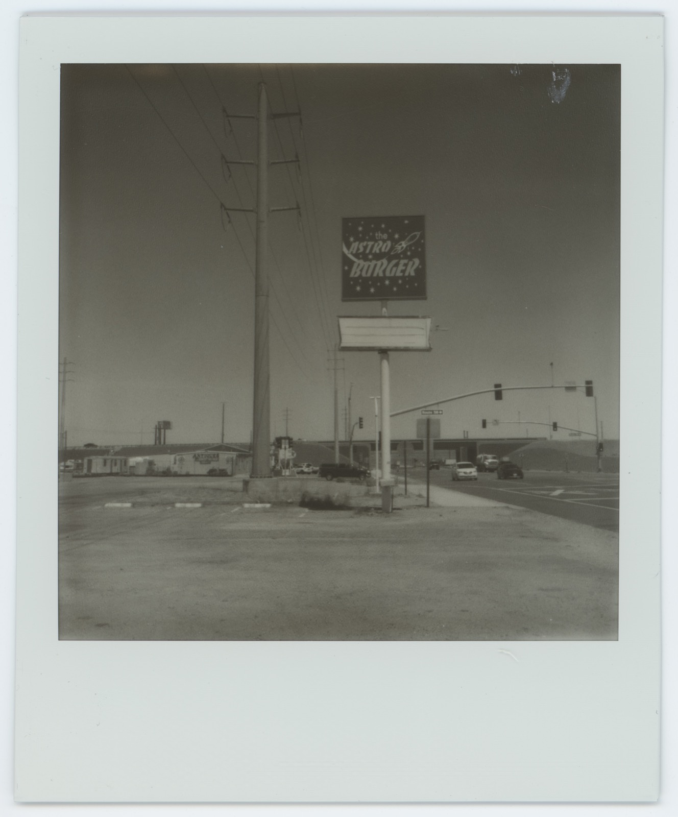 Polaroid: the freestanding Astro Burger road sign and a power pole, distant traffic lights and low buildings.